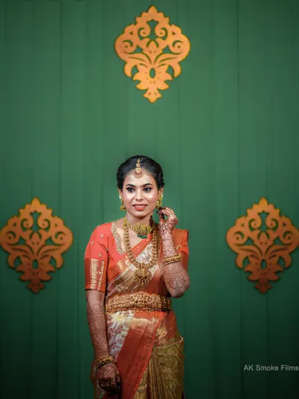 A beautiful bridal portrait against a simple green wall with gold motifs, making her orange saree pop.