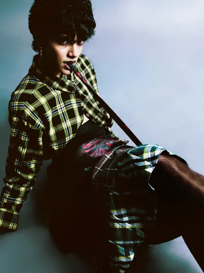 A seated portrait from 'My Flatmate's Wardrobe,' with the model in a layered plaid outfit. The pose is casual yet confident, perfectly capturing the essence of personal style.