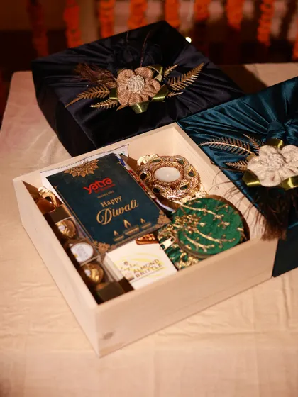 A wooden box hamper curated for Yatra, filled with chocolates, a candle holder, and other festive treats, all presented with a branded Diwali card.
