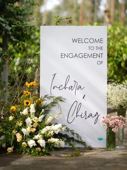 The welcome signage for Inchara and Chirag's engagement featured elegant calligraphy on a clean white board. It was accented with arrangements of sunflowers, baby's breath, and other fresh blooms to greet guests warmly.