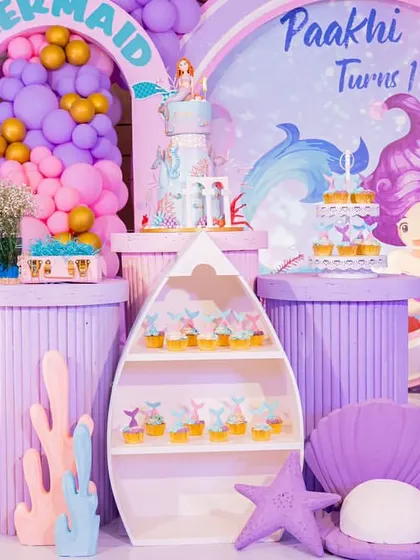 A detailed view of the mermaid party dessert station, featuring a themed cake, cupcakes displayed in a boat-shaped shelf, and various underwater props.