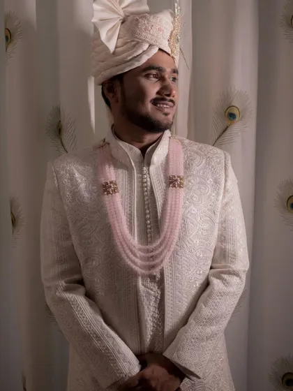 A portrait of the groom, Rahul, looking elegant in a classic ivory sherwani with a pink beaded necklace.