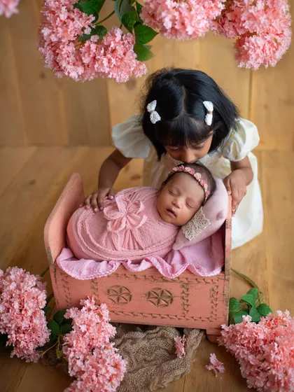 A big sister peeking over the crib at her sleeping newborn sister. This floral-themed setup with the pink cradle is perfect for celebrating two girls.