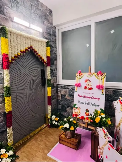 A beautiful entrance for a housewarming ceremony. The door is framed with intricate flower garlands, and a welcome sign with cow statues adds to the traditional and warm welcome.