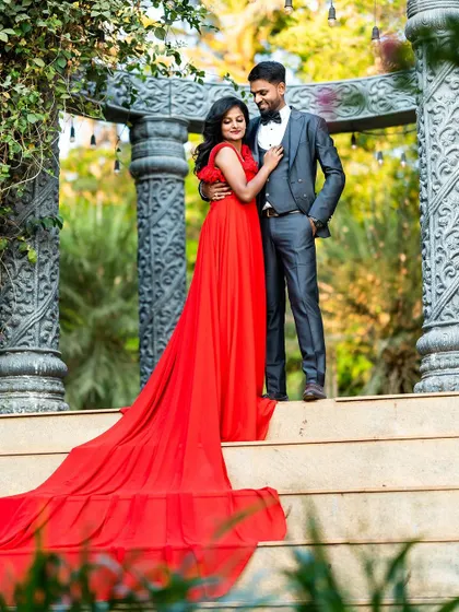 A romantic pre-wedding photo on a grand staircase, with the groom in a suit and the bride in a flowing red gown, capturing a classic, elegant moment.