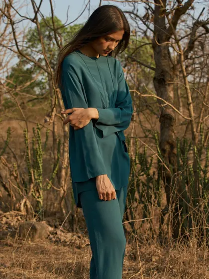 A fashion portrait set in a dry, wooded landscape. The deep teal of the outfit stands out beautifully against the natural, earthy tones of the environment.