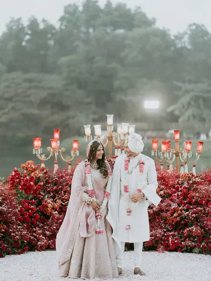 The couple stands before a wall of red blooms, a simple yet powerful statement of love and passion. The natural greenery in the background provides a beautiful contrast.