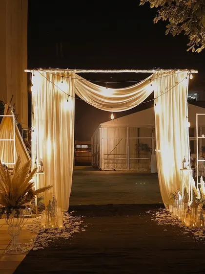This simple yet elegant draped entranceway creates a soft and romantic welcome to an outdoor event. Lined with scattered petals and pampas arrangements, it sets a serene and inviting tone for the evening.