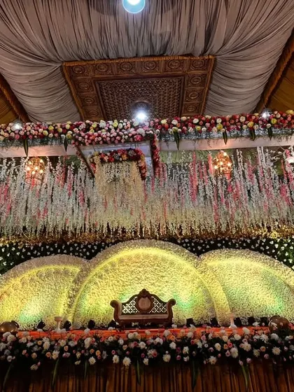 A classic reception stage with a massive, arched floral backdrop. The warm lighting highlights the thousands of flowers used, creating a rich and opulent atmosphere for a truly grand wedding.