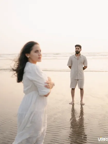 An artistic shot with the bride-to-be in focus in the foreground, and her partner standing in the background by the ocean. This composition creates depth and tells a story of connection and distance.