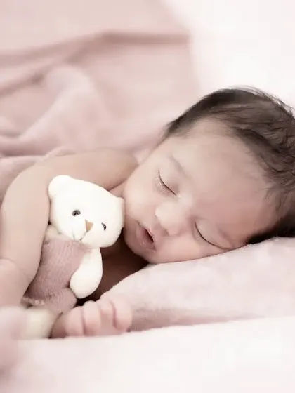 A tender moment as a sleeping newborn cuddles a tiny teddy bear. The soft pink tones of the blanket and the gentle lighting create a warm and dreamy atmosphere.