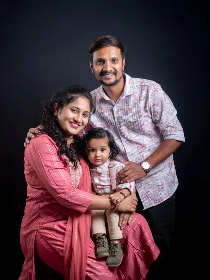 A warm family portrait against a dark studio background. The focused lighting creates an intimate feel, drawing attention to the family's close bond.