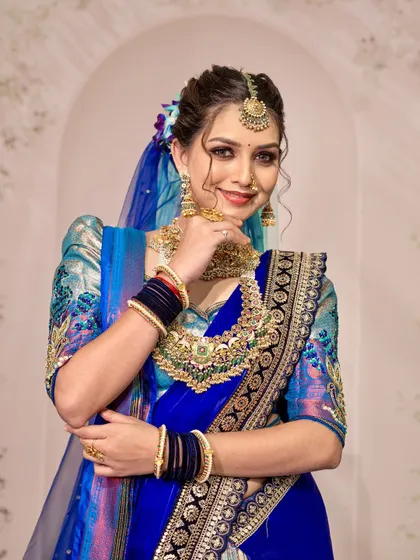 A peacock-inspired bridal look. The royal blue saree is draped with a unique pallu style and a sheer blue veil to mimic the beauty of a peacock's feathers.