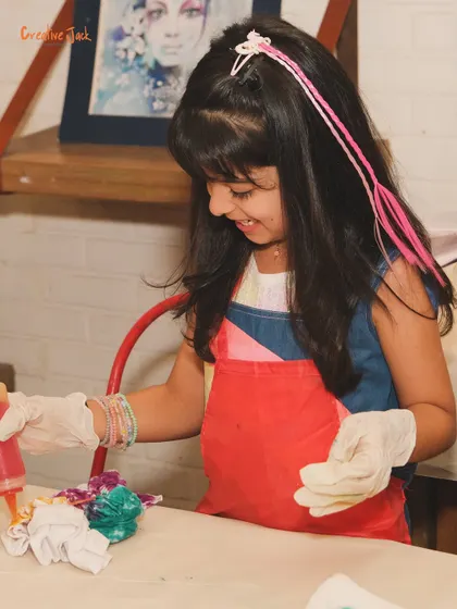 A smiling girl enjoys a tie-dye activity at a birthday party, her hair decorated with a pink extension as she creates.