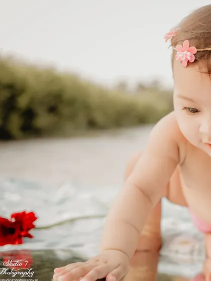 A close-up shot from the same outdoor birthday session, focusing on the baby's curious expression. The soft focus on the background keeps the attention on her, highlighting her delicate features and the floral headband.
