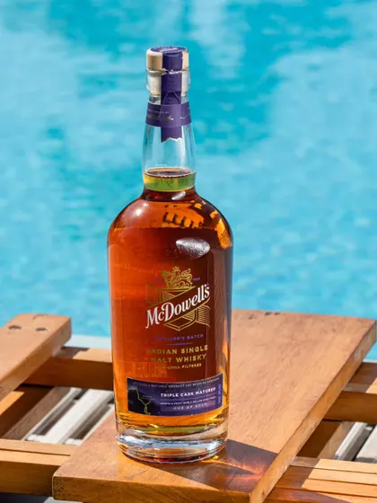 A lifestyle shot of the McDowell's bottle by a swimming pool. This places the product in a relaxed, leisurely, and aspirational setting.