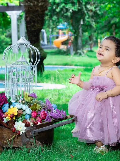 A joyful moment in the park, with this little girl in a beautiful purple dress surrounded by flowers.