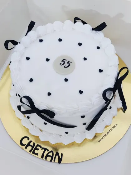 A vintage-style cake for a 55th birthday. The simple white design with black polka dots and delicate ribbon bows creates a classic and timeless look.