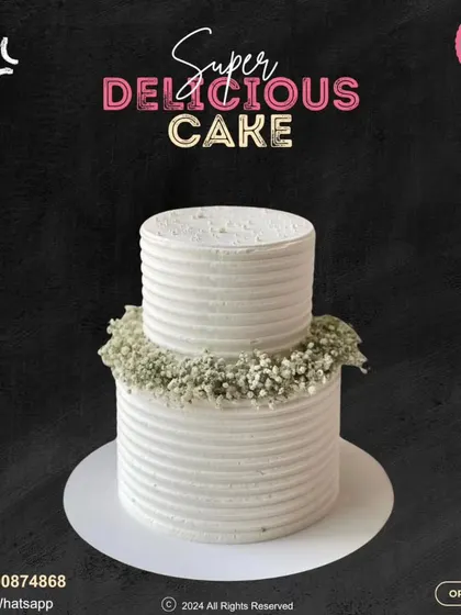 An elegant two-tier cake perfect for a wedding or anniversary. The clean, ribbed white frosting is beautifully accented with a wreath of delicate baby's breath flowers.