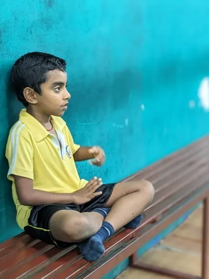 A young player takes a moment to rest and observe on the sidelines. We balance intense training with necessary breaks to ensure focus and prevent fatigue.