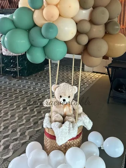 A hot air balloon centerpiece featuring a teddy bear, perfect for a baby shower or first birthday. The balloon is made of sage green and beige balloons, creating a soft and dreamy look.