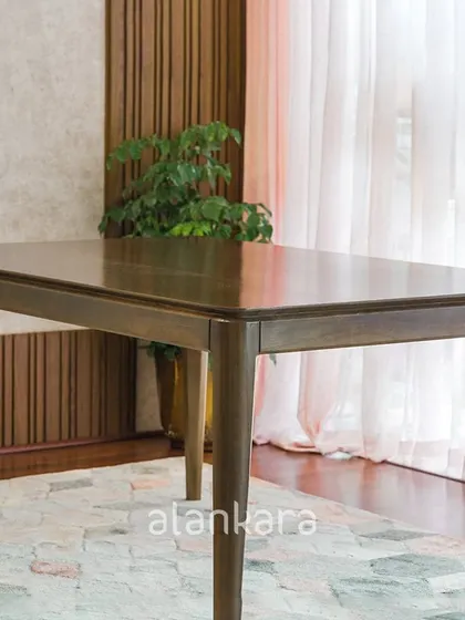 A focus on the Zircon dining table itself, emphasizing its sleek profile and the quality of the teak wood, set against elegant paneled walls and sheer curtains.
