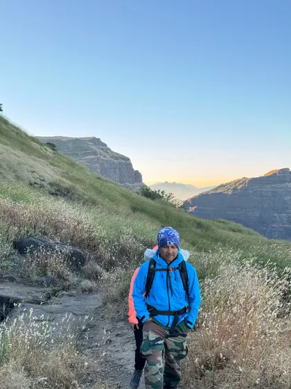 A hiker on the trail at Ratangad, with the golden light of dawn illuminating the Sahyadri range. The terrain is rugged and beautiful.