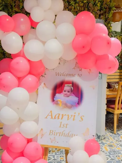 The personalized welcome sign for Aarvi's party, featuring a beautiful photo and surrounded by matching pink and white balloons.