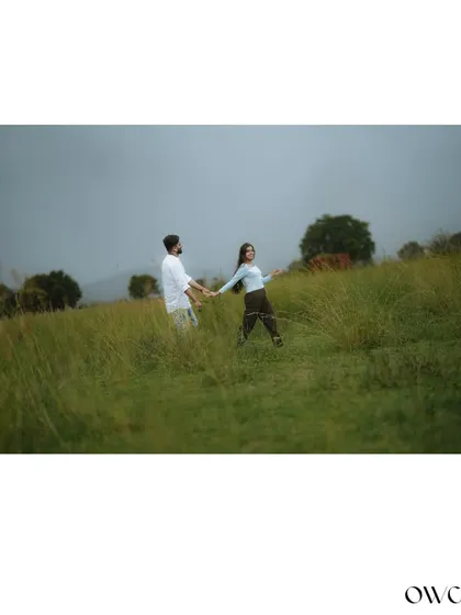 A scenic wide shot of a couple holding hands in a vast green meadow, emphasizing their connection within a grand landscape.