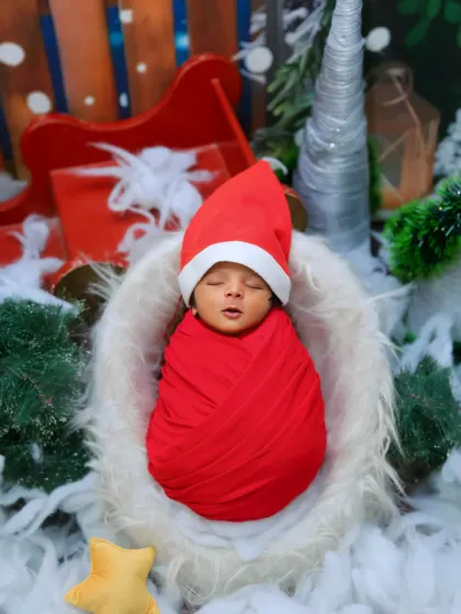 A festive Christmas-themed newborn photo. The baby is swaddled in red and wearing a Santa hat, nestled in a sleigh setup complete with snow and presents for a perfect holiday memory.