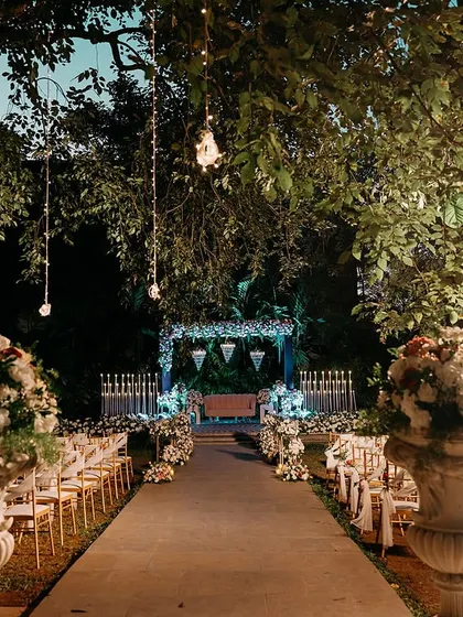 A beautifully lit evening aisle for an outdoor reception, flanked by large floral urns and leading to a candle-lit stage.