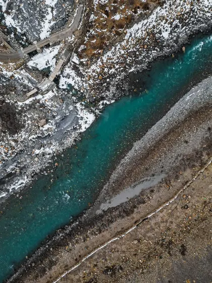 A top-down aerial shot of the turquoise river in Poh, contrasting with the snow and rocky banks.