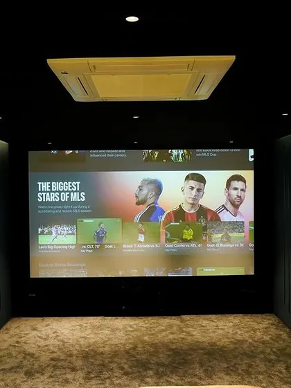 A direct view of the screen from the front of the room, showcasing the empty space before the seating. This highlights the scale of the room and the professional installation of the screen and speakers.