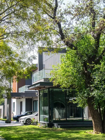 At Triveni Farmhouse, the architecture is nestled among mature trees. The home's modern design, with its glass-wrapped corner and cantilevered balconies, creates a beautiful contrast with the organic forms of the surrounding nature.
