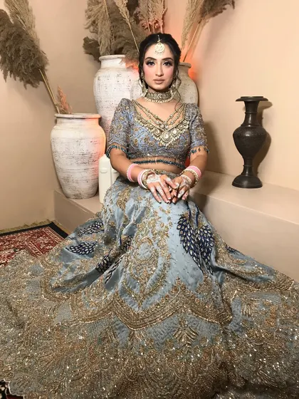 A full-length portrait showing the grandeur of the powder blue lehenga with peacock motifs. The makeup is kept soft and romantic to balance the ornate outfit.