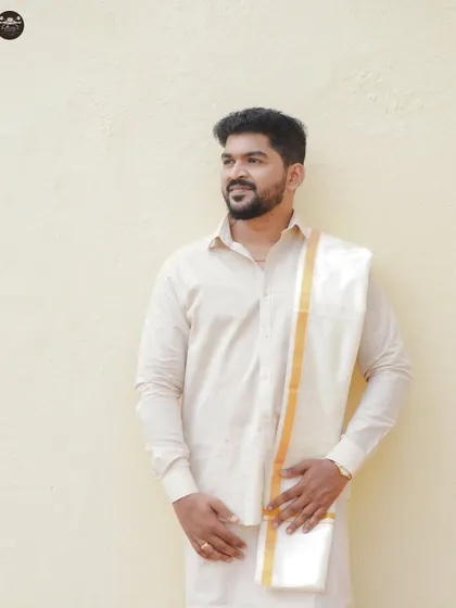A handsome portrait of a groom dressed in a traditional South Indian white shirt and veshti with a golden border. This shot highlights the simple elegance of the groom's wedding day look.