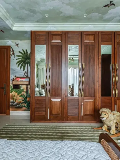 This view shows the expansive wooden wardrobe with mirrored panels, designed to make the room feel larger and reflect the beautiful jungle mural. Every piece of furniture was crafted to feel part of this enchanting world.