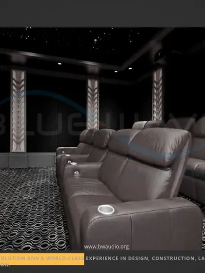 A sophisticated modern theater with plush leather sofa-style recliners and decorative, backlit wall columns. The patterned carpet and dark color scheme contribute to a polished and high-end aesthetic.