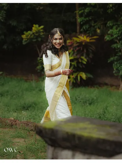 A happy bride walks through a green field, her kasavu saree glowing in the light.