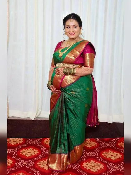 A full-length view of a traditional baby shower look. The client is glowing in her green silk saree, with makeup that is classic, festive, and comfortable.