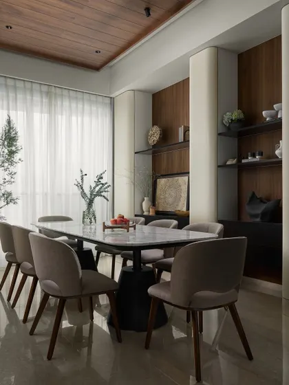 In the dining room, vertical curved storage units blend seamlessly into the walls. The warm wooden backdrops in the display niches add depth, while our custom "Hover" dining table creates a sense of lightness and grandeur.
