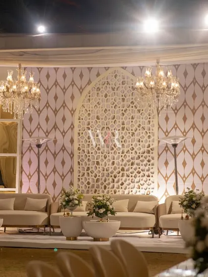 The main lounge area, featuring a custom-designed backdrop with a central jaali arch and mirrored panels. The space is softened with plush ivory sofas and chandeliers, creating a mood of intimate luxury.