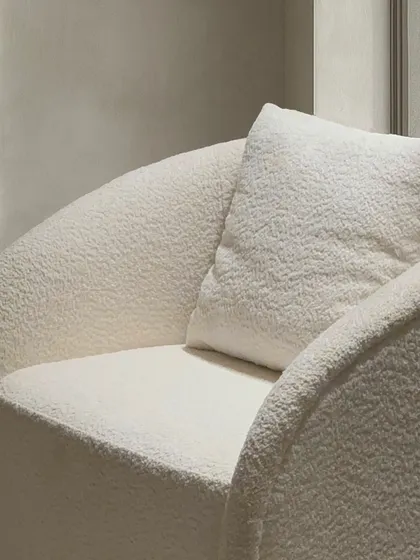 A detailed view of the barrel-back armchair, focusing on the rich, looped texture of the bouclé fabric. This material choice was intentional, designed to soften the chair's simple, geometric form and add a layer of tactile warmth.