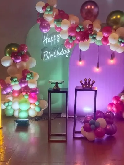 A stylish and modern first birthday setup with neon signs, arch backdrops, and a unique color scheme of magenta, green, and white.
