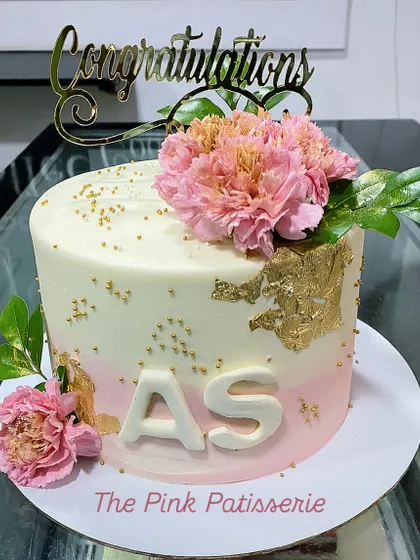 A lovely congratulations cake with a pink ombre effect, gold leaf, and fresh pink carnations. The design is personalized with the initials "AS" in white fondant.