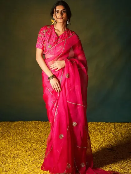 A vibrant fuchsia organza saree that makes a bold statement. The scattered floral motifs and sheer fabric create a look that is both festive and light, perfect for a summer wedding.