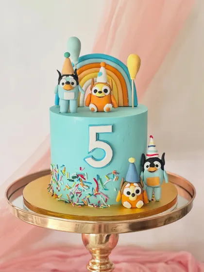 This bright and cheerful Bluey-themed cake is perfect for a fifth birthday. It features the whole Heeler family in party hats, with a colourful rainbow and sprinkles on a sky-blue buttercream base.