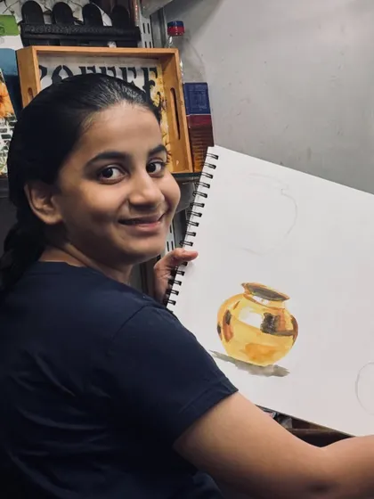 Nothing makes us happier than seeing a student proud of their progress. Here, a student from our elementary batch shows off her beautifully rendered metal pot, mastering light and shadow.