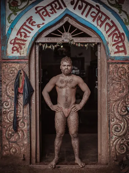 A wrestler stands proudly at the entrance of the Shri Shahu Vijayi Gangavesh Taleem, his body covered in the training mud. This powerful stance captures the pride and dedication of a Kolhapuri Pailwan.