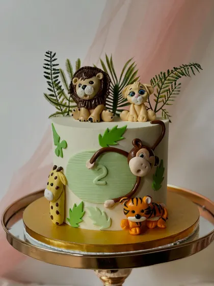 A safari cake for a second birthday, complete with a swinging monkey. This design features a lion, lion cub, tiger, and giraffe, all set against a backdrop of fondant jungle leaves.